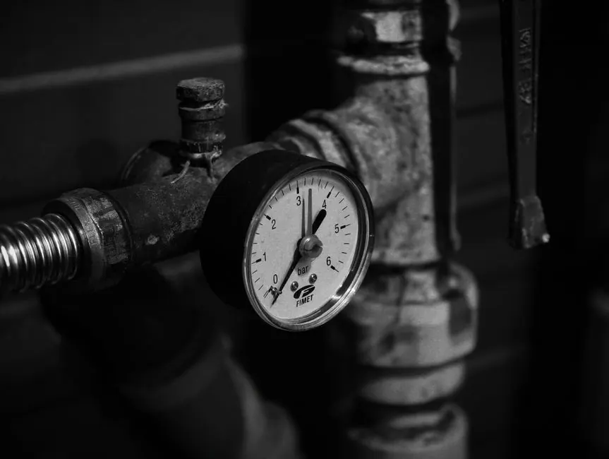 Close-up of a vintage pressure gauge on industrial pipes in monochrome.
